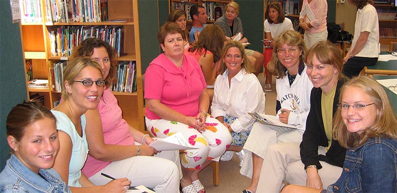 A group of eight smiling teachers working together.