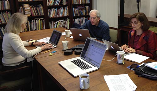 Three researchers at laptops in a library.
