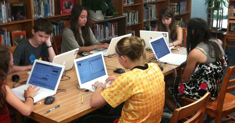 Five students work at laptops in a library